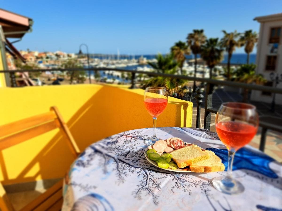 Terrasse von Follow the Sun mit zwei Gläsern Roséwein und Blick über den Hafen von Portoscuso aufs Meer