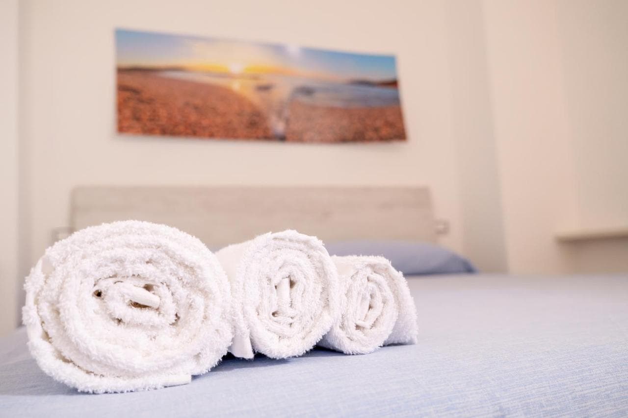 Helles Schlafzimmer mit frisch gerollten Handtüchern auf dem Bett und einem Strandbild über dem Kopfteil