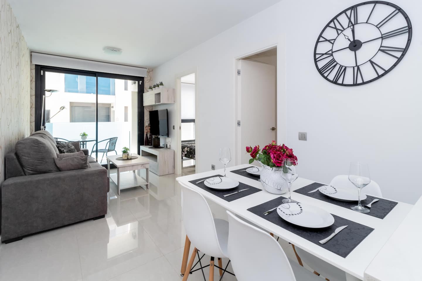 Heller Wohn- und Essbereich mit grauem Sofa, weissem Esstisch und grosser Wanduhr im Apartment in Torrevieja