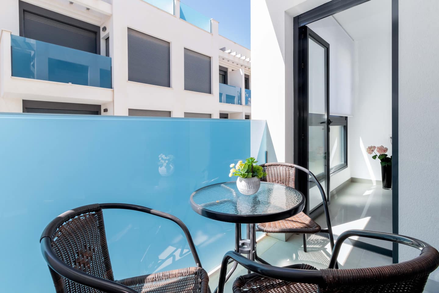 Balkon mit Bistrotisch und Korbstühlen, Blick auf die moderne Wohnanlage